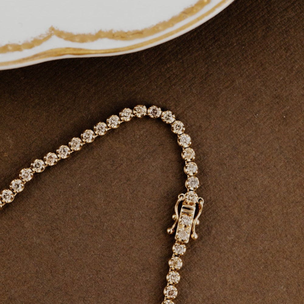 Diamond champagne tennis necklace on a brown surface with a decorative edge.