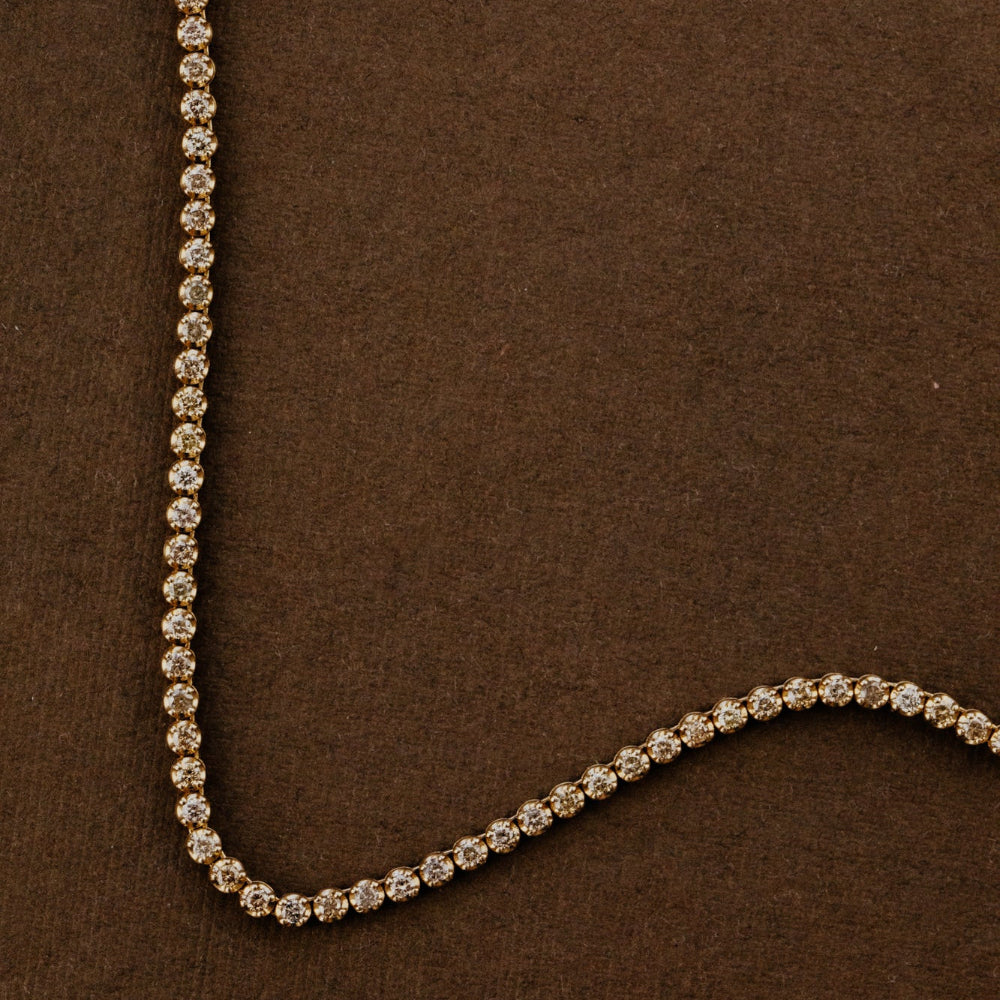 Champagne diamond tennis necklace on a brown background.