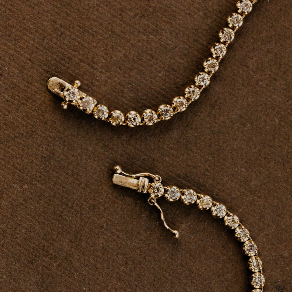 Gold champagne diamond tennis necklace on a brown textured surface.