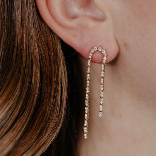 Close-up of an ear wearing a curved pave diamond dangle earring.