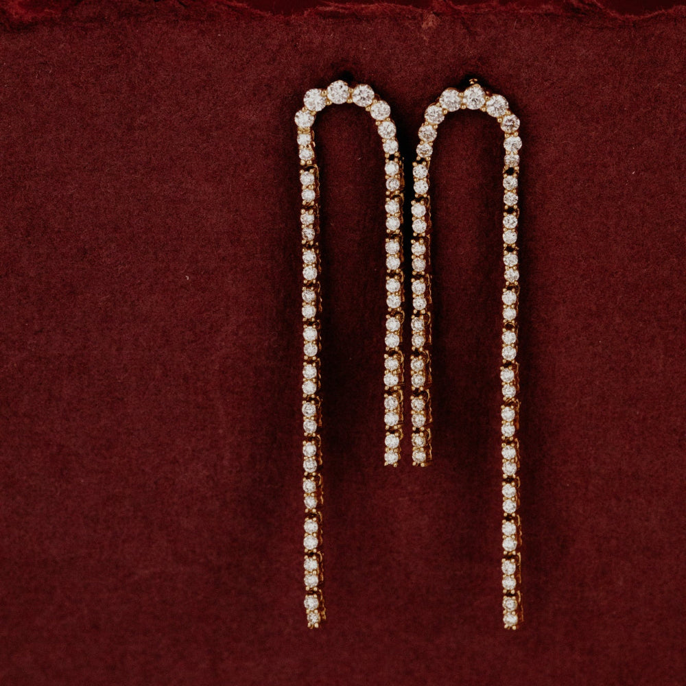 Pair of curved pave diamond dangle earrings on a burgundy background.