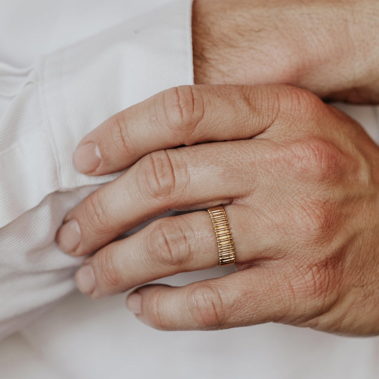 Close-up of a man's hand wearing a gold Drew wedding band on a light background.