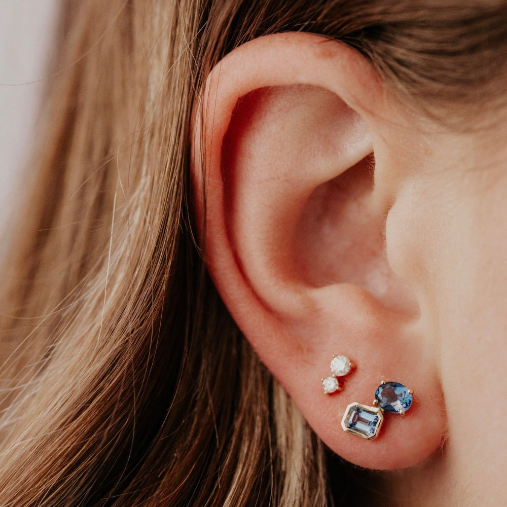 Close-up of an ear wearing two earrings with gemstones.