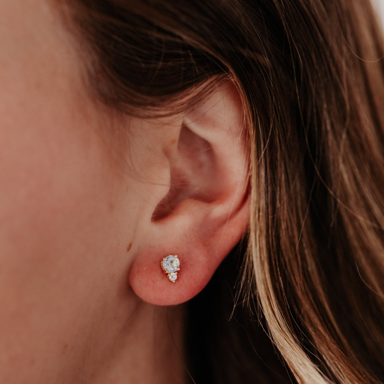 Close-up of an ear wearing a aquamarine and diamond earring with blurred background