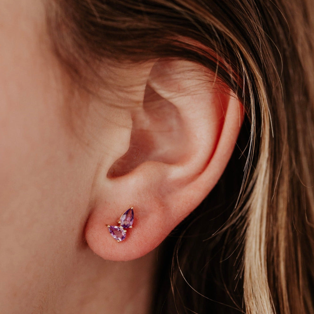 Close-up of an ear wearing a purple pear earring with blurred background