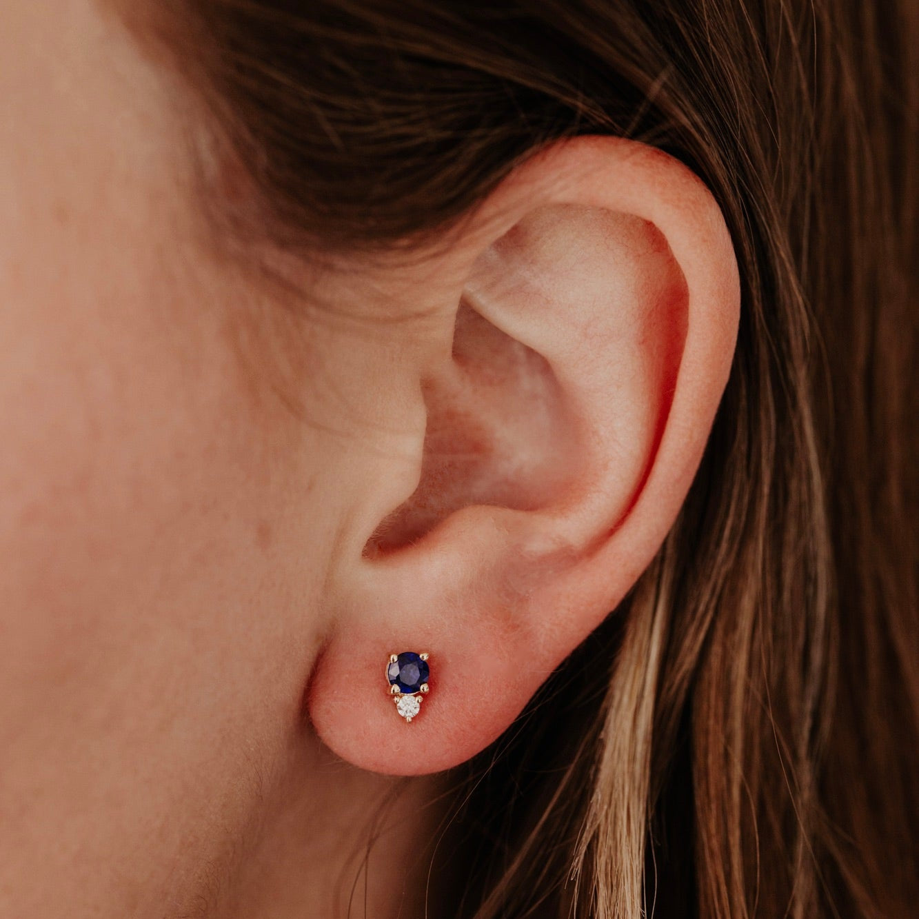 Close-up of an ear wearing a blue sapphires gemstone earring with a blurred background
