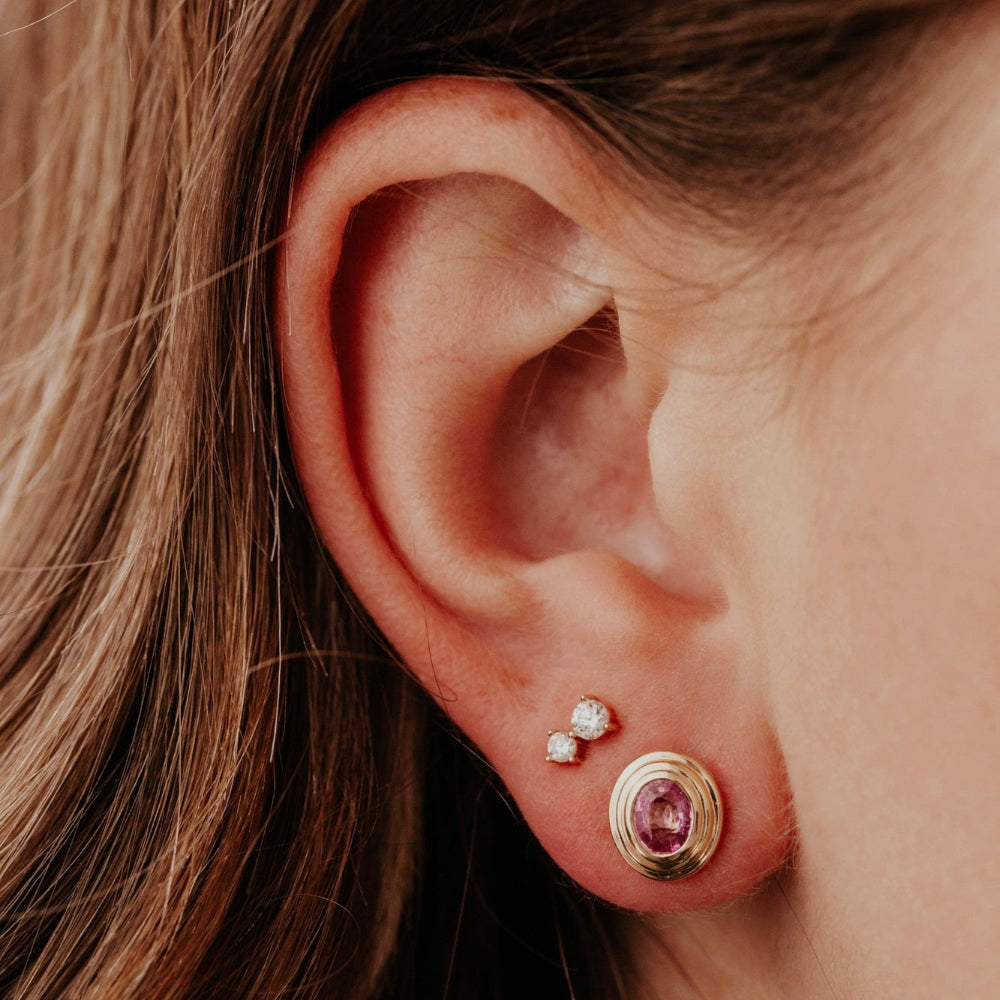 Close-up of an ear wearing a gold earring with a pink gemstone.