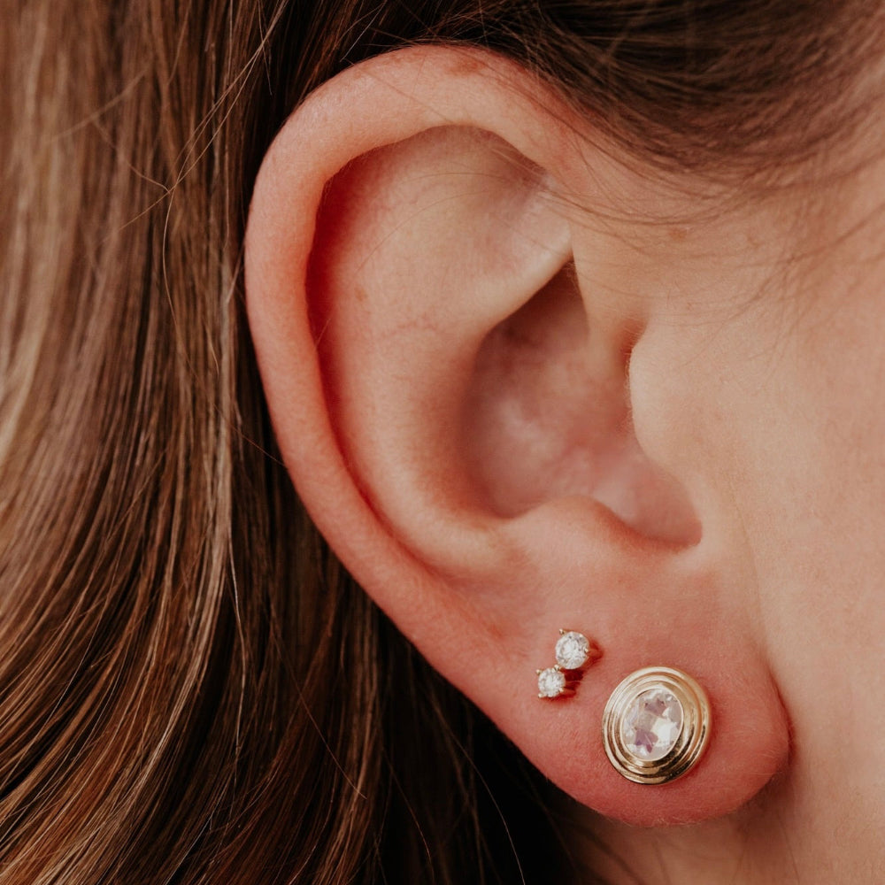 Close-up of an ear wearing two gold earrings with gemstones.