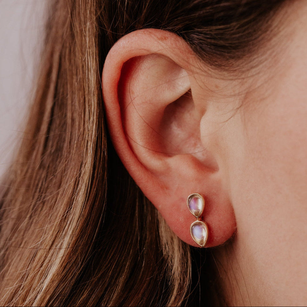 Close-up of an ear wearing a gold earring with a moonstone gemstone.