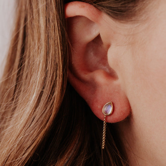 Close-up of an ear wearing a gold earring with a moonstone gemstone and front-to-back chain.