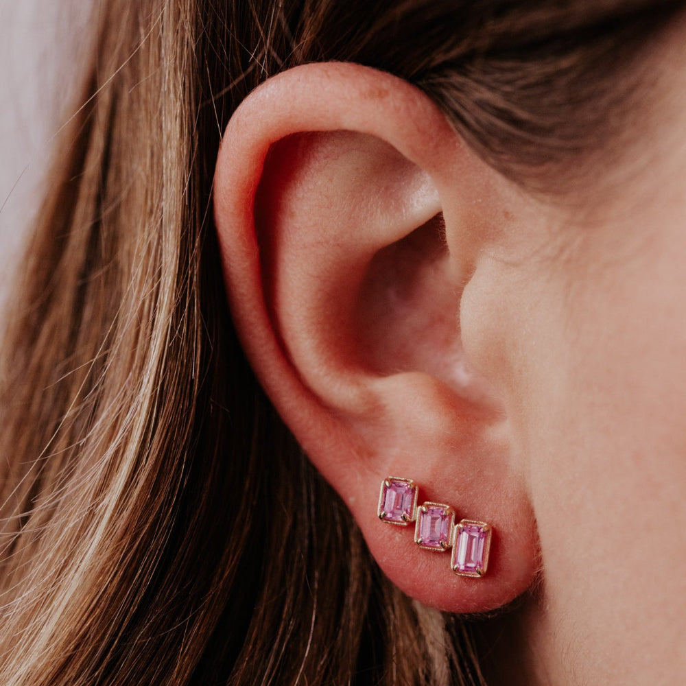 Close-up of an ear wearing pink gemstone earrings with a neutral background
