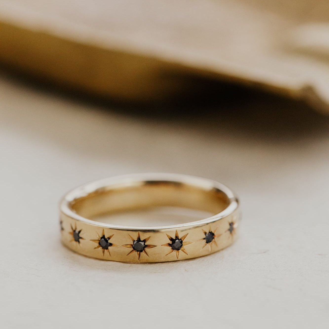 Gold Estelle wedding band with star-shaped black diamonds on a neutral background.