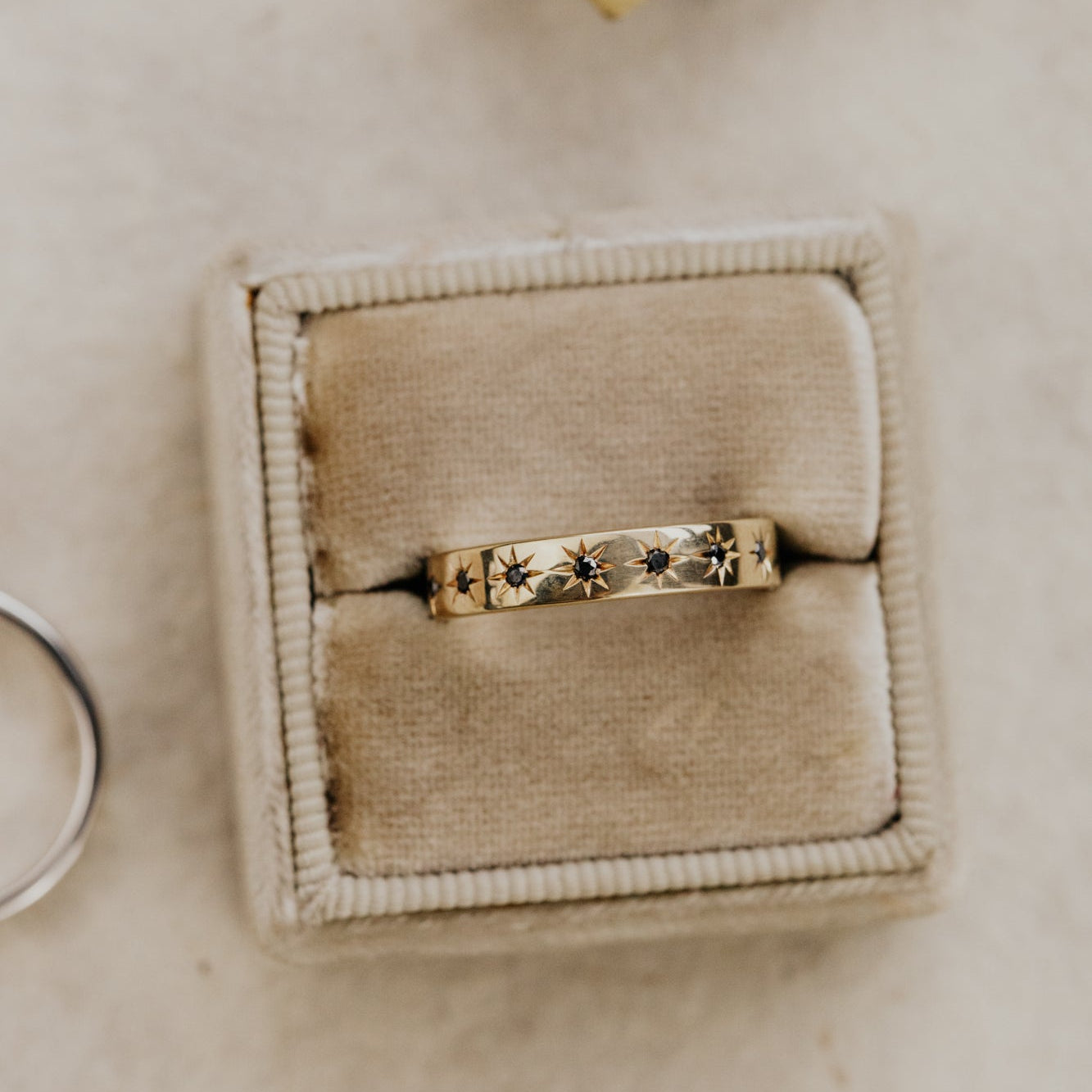 Yellow gold Estelle band with black diamonds set in a star designs in a beige jewelry box on a light background.