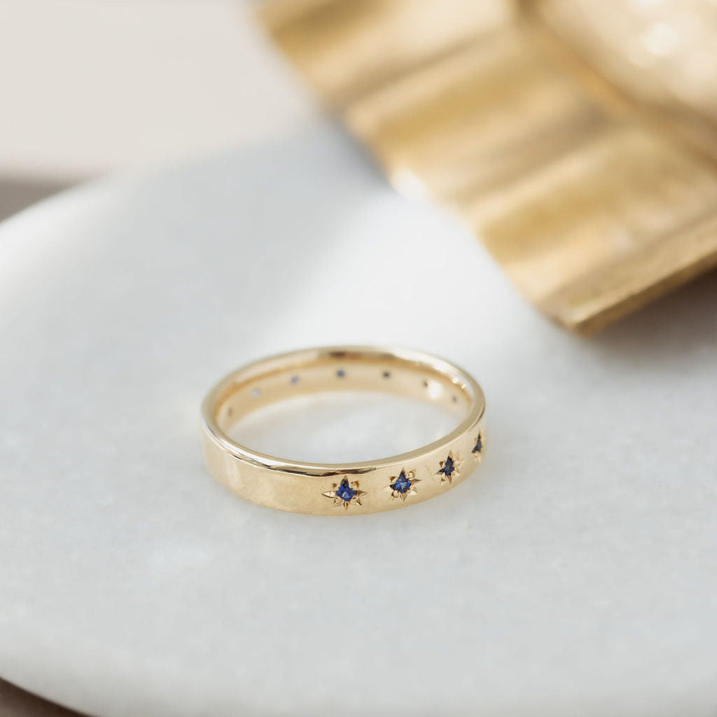 Yellow gold Estelle band with embedded blue sapphires on a white surface.
