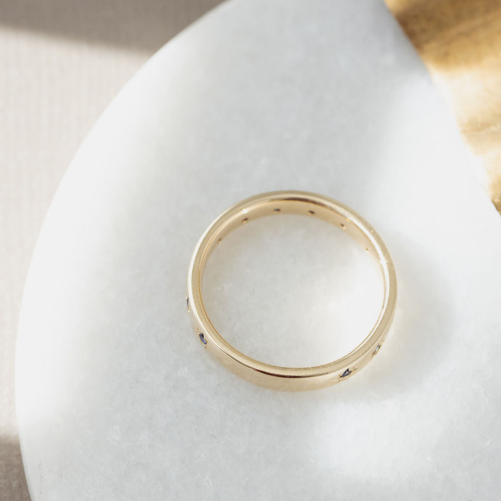 Gold Estelle blue sapphire band on a white ceramic dish with a soft background.