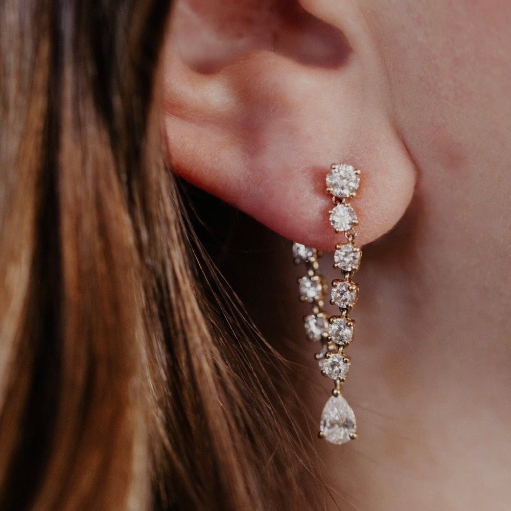 Close-up of a person wearing elegant front to back diamond earrings with a blurred background.