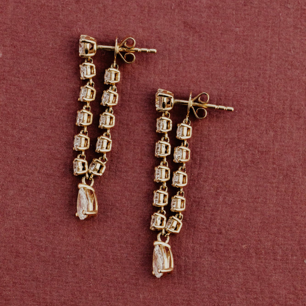 Gold earrings with diamonds stones on a maroon background.