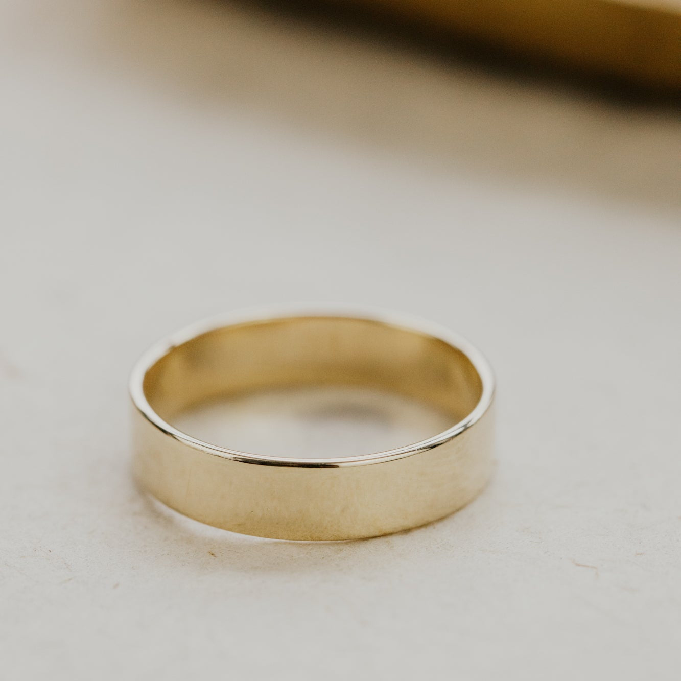Yellow gold stacker band on a light beige surface.