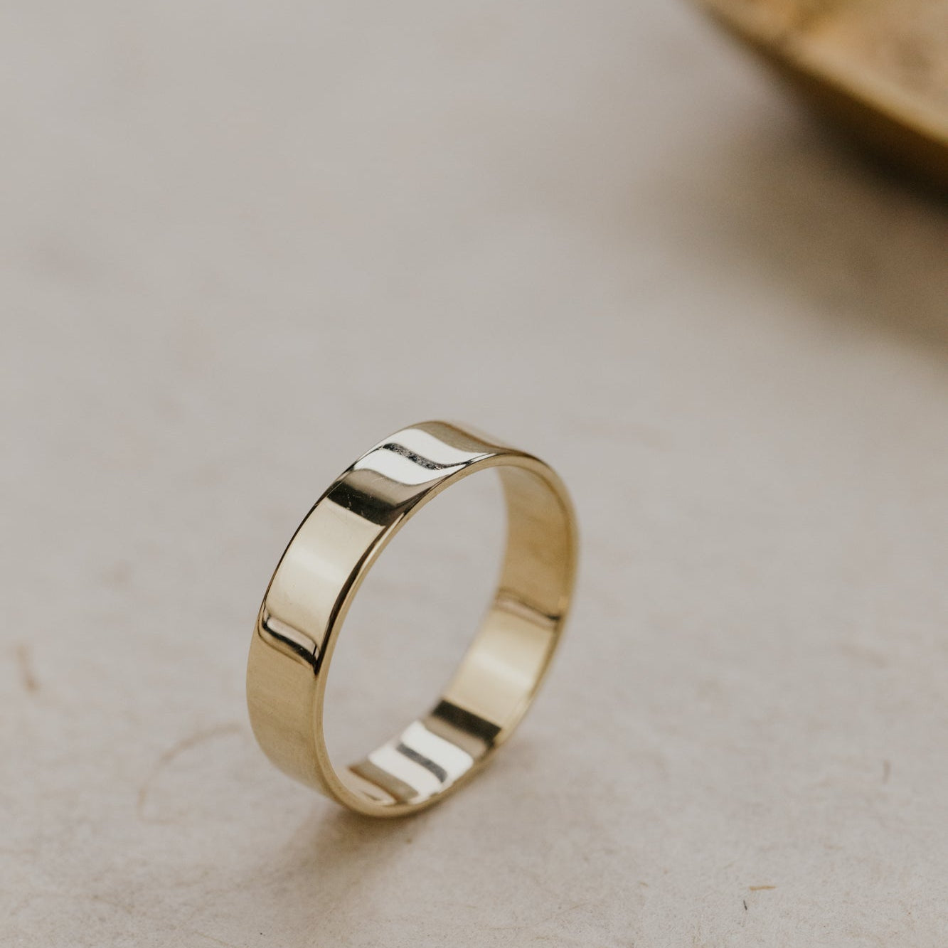 Yellow gold stacker band on a light beige surface.