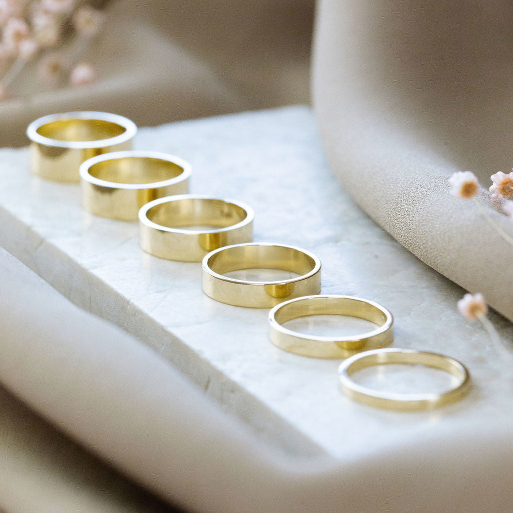 Set of gold stacker bands lined up by size on a marble surface with a soft background.