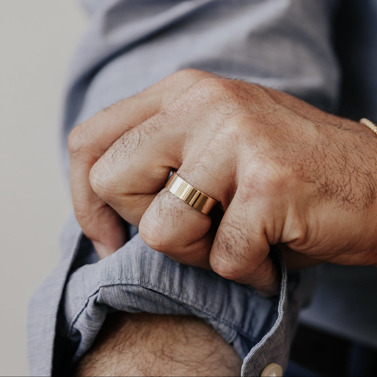 Close-up of a man's hand wearing a gold stacker band with a blurred background.