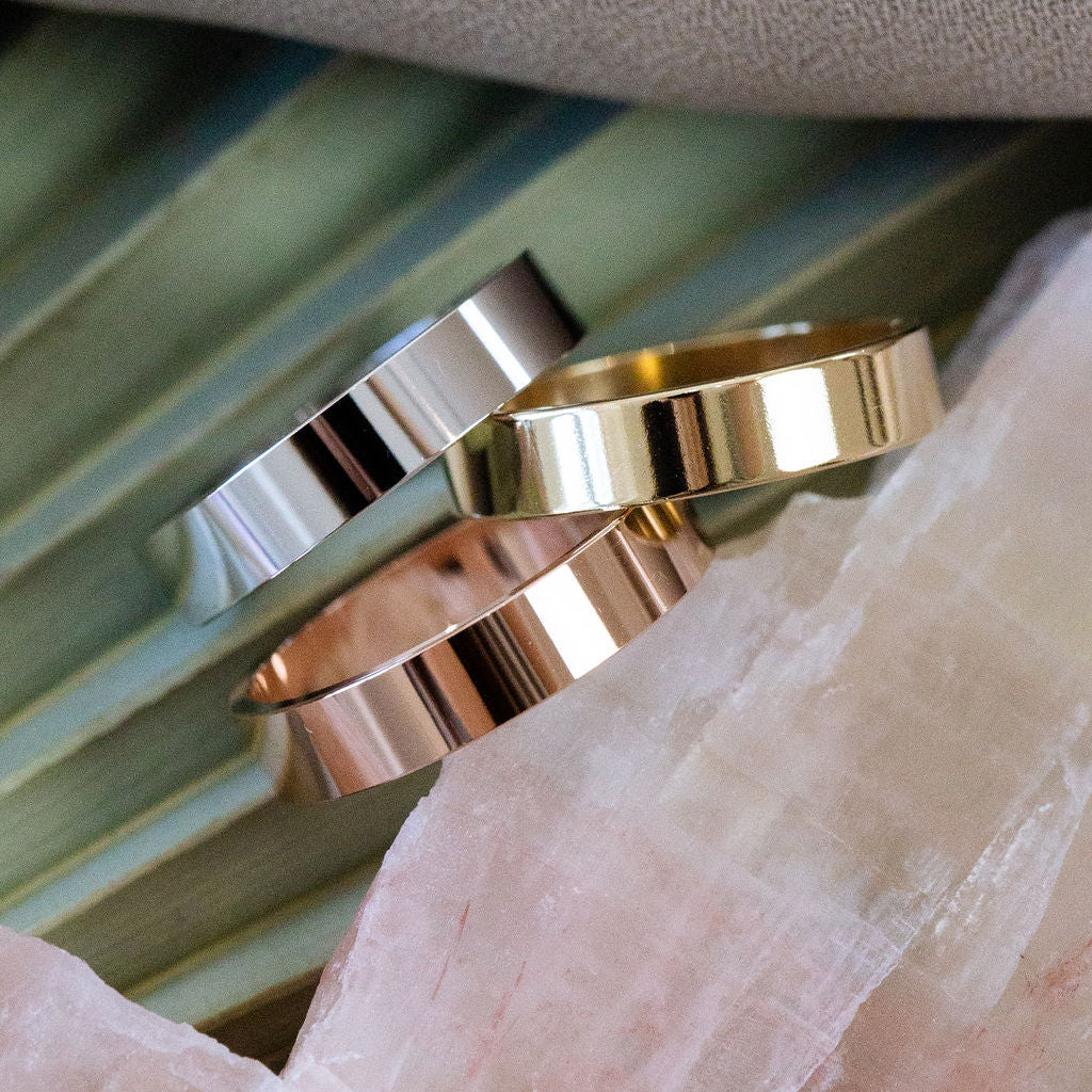 Three gold stacker bands in yellow, white, and rose gold on a textured surface.