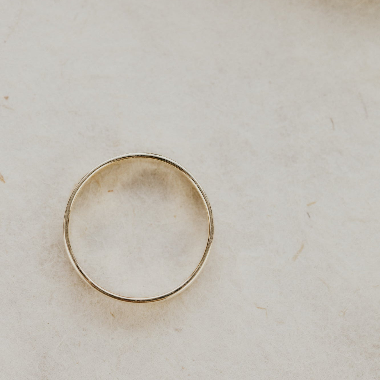Yellow gold stacker band on a light beige background.