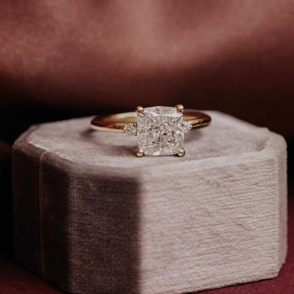 Isla cushion diamond engagement ring on a textured surface with a dark background.