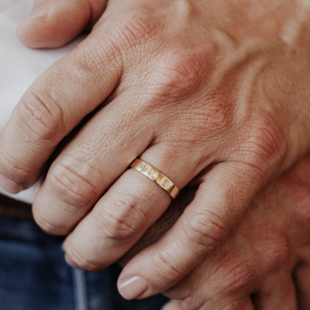 Close-up of a man's hand wearing the Jaden gold wedding band with three baguette diamonds.