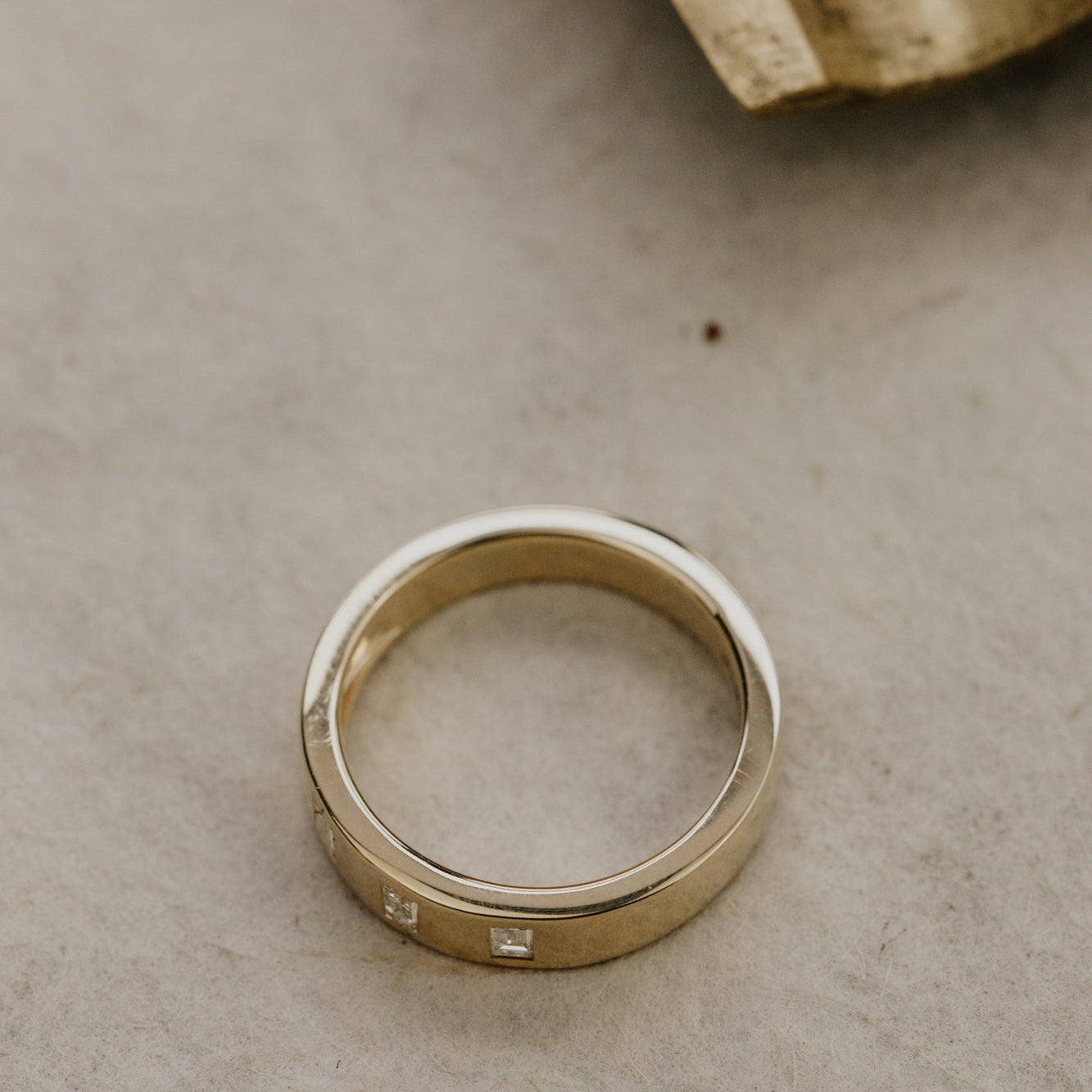 The Jaden gold wedding band with embedded diamonds on a textured surface.