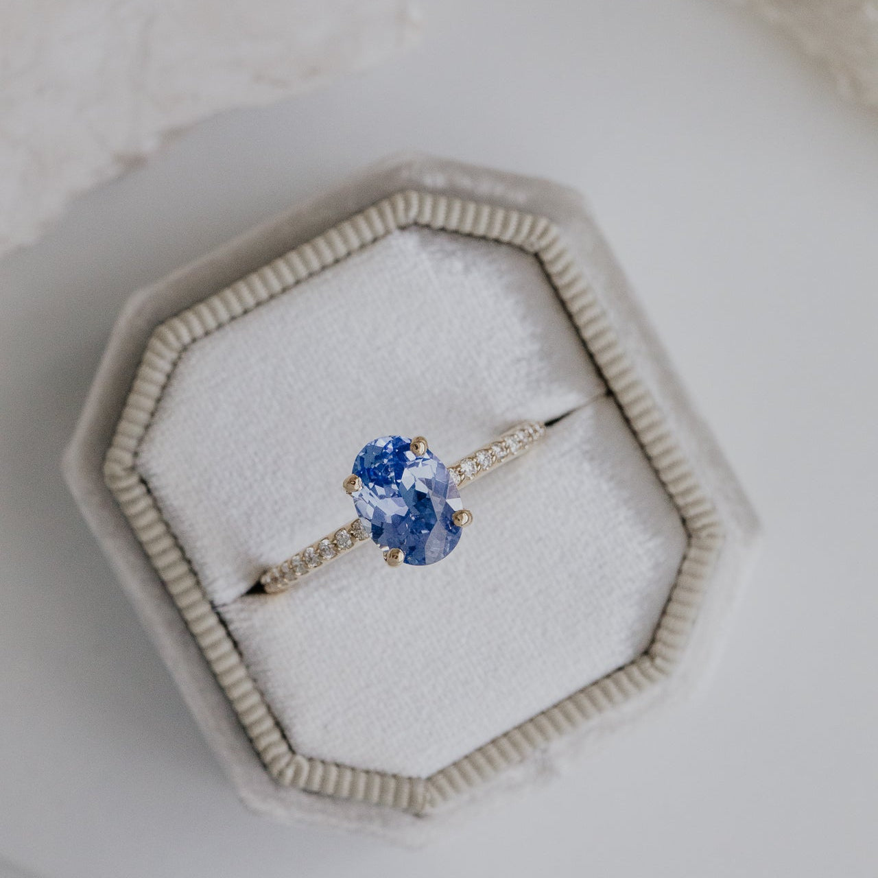Jenna engagement ring with a blue oval sapphire in a hexagonal jewelry box on a light background.