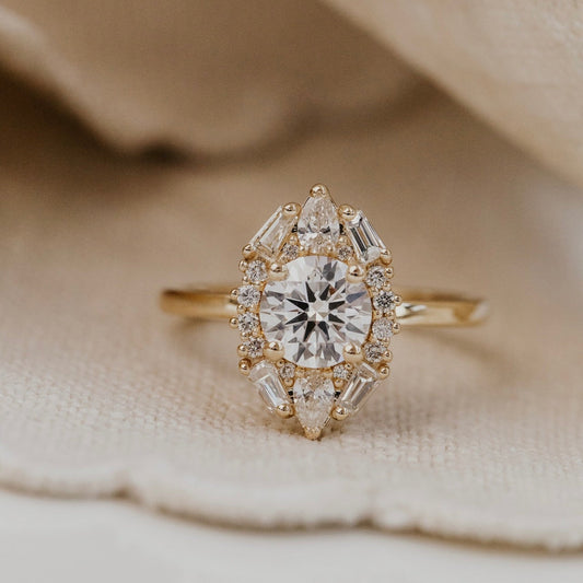 The Lori round diamond ring with a diamond halo on a beige fabric background.