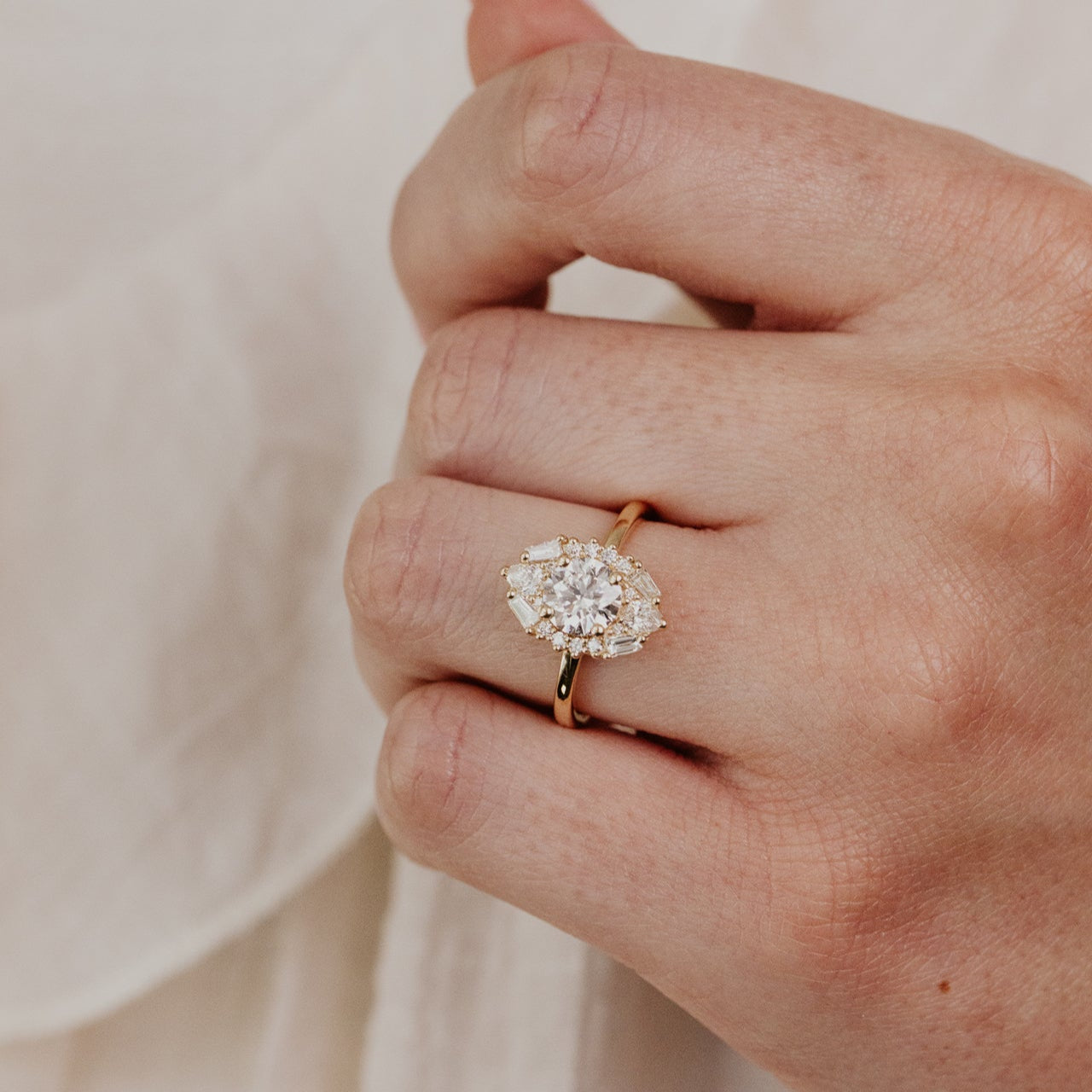 Close-up of a hand wearing a yellow gold  Lori round diamond engagement ring against a neutral background.