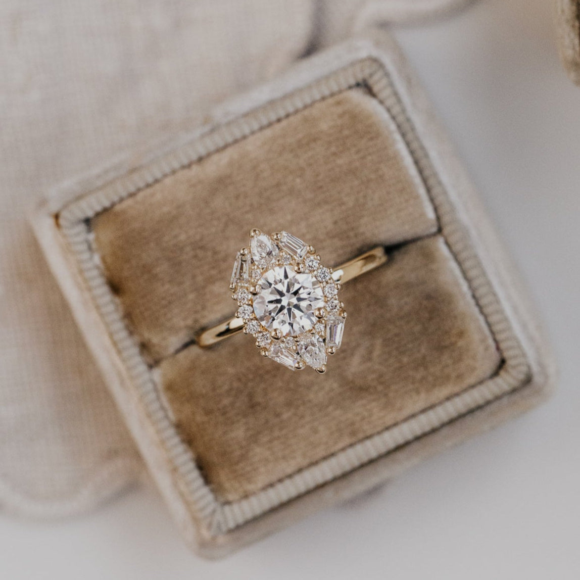 Lori round diamond engagement ring with diamond halo in a beige velvet box on a light background.