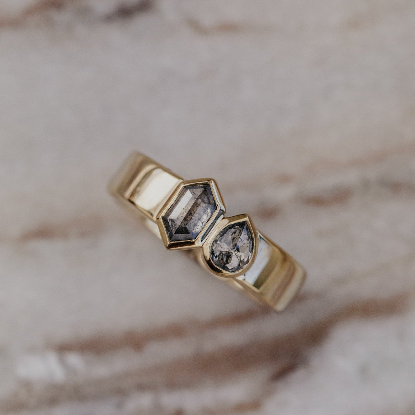 Gold Madison ring with two gray rustic diamonds on a marble surface.