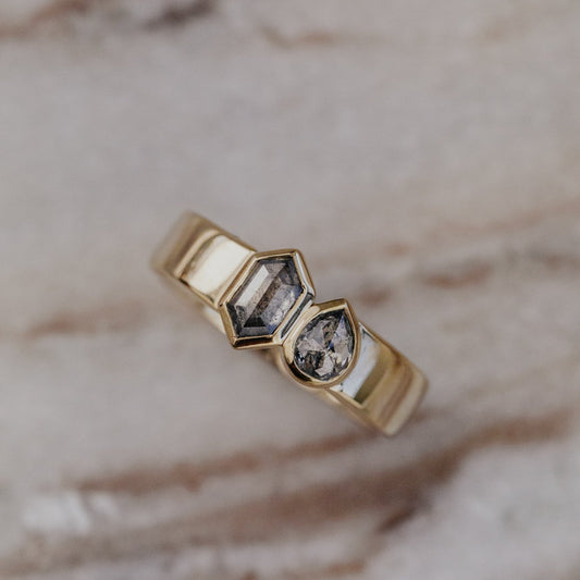 Gold Madison ring with two gray rustic diamonds on a marble surface.
