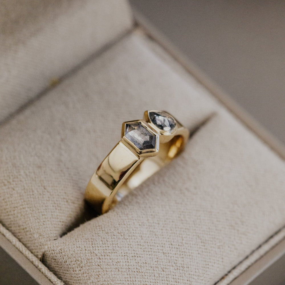 Gold Madison ring with hexagon and pear rustic diamonds on a beige cushion in a jewelry box.
