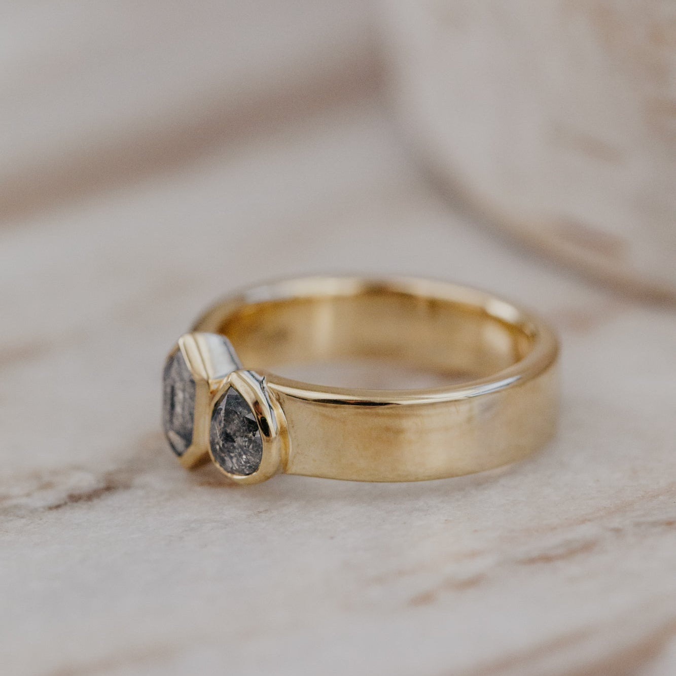 Gold Madison ring with gray rustic diamonds on a marble surface.