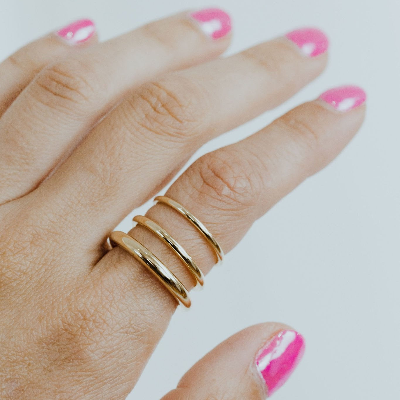 Close up of a hand wearing three Maeve gold bands in different widths on a white background.