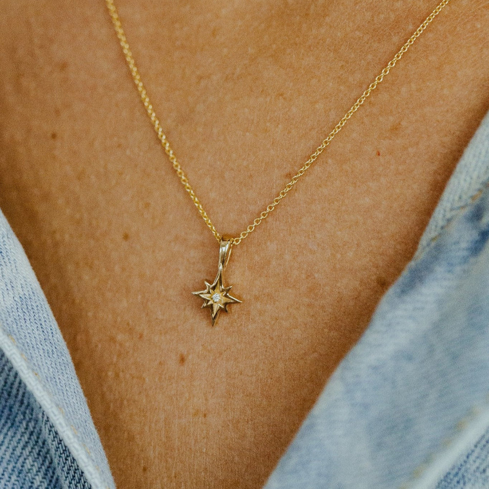A person wearing a denim jacket with a gold necklace featuring a star-shaped charm pendant and a small diamond in the center visible against the neckline.