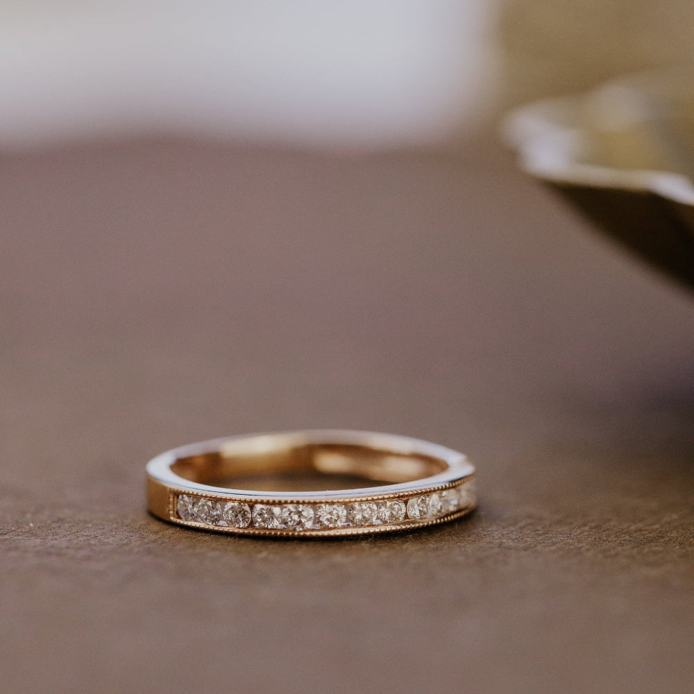 Rose gold wedding band with round diamonds set in a channel on a brown surface