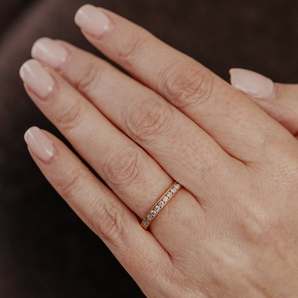 Close-up of a hand wearing a rose gold wedding band with diamonds on a dark background.