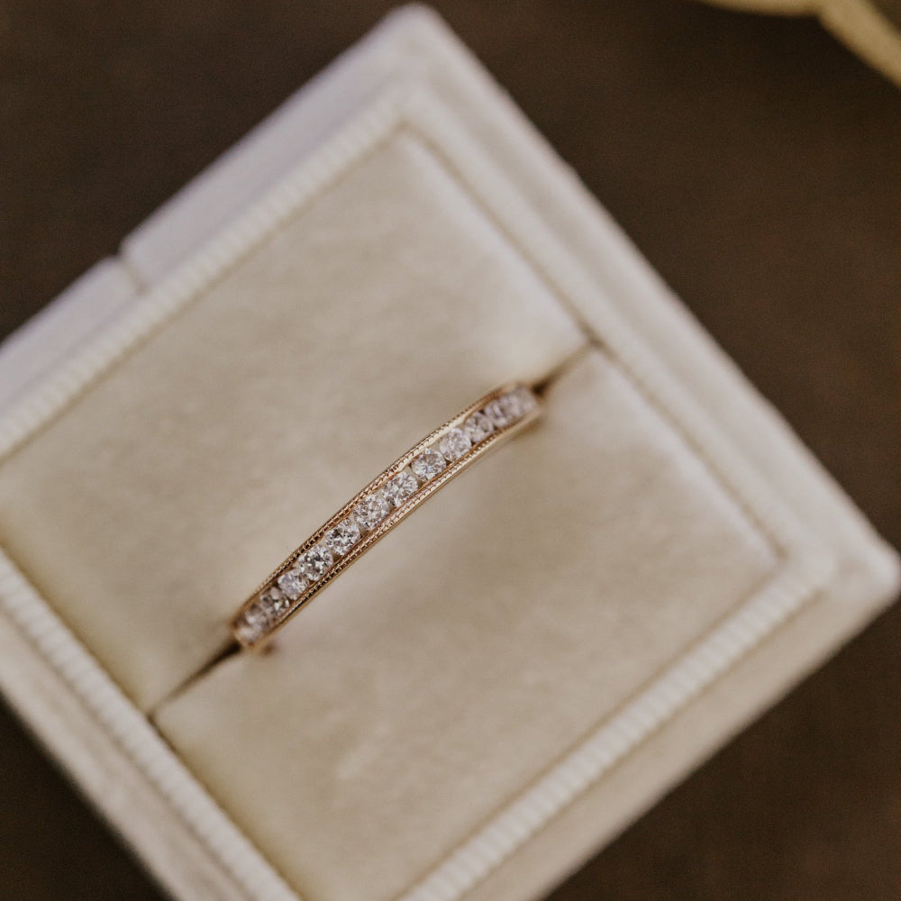 Rose gold wedding with channel set diamonds in a beige jewelry box on a dark surface.