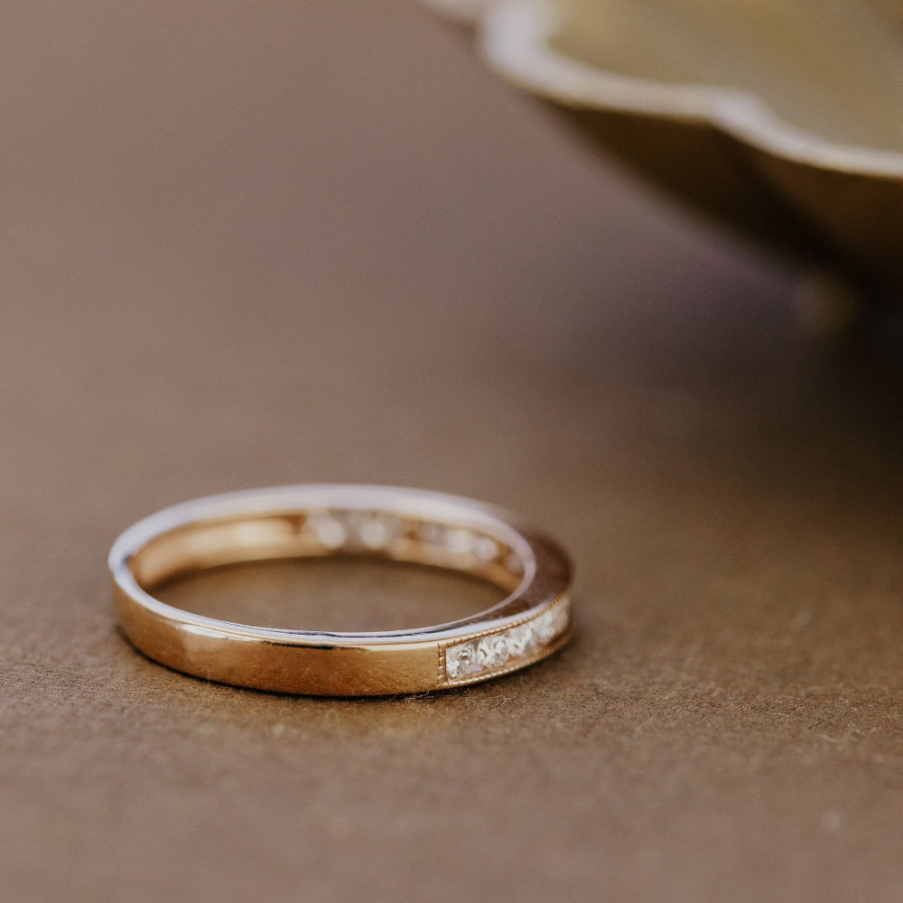 Rose gold wedding band with round diamonds on a brown surface.
