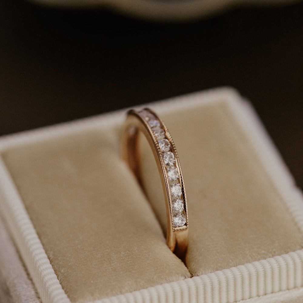 Rose gold wedding band with diamonds in a beige jewelry box.