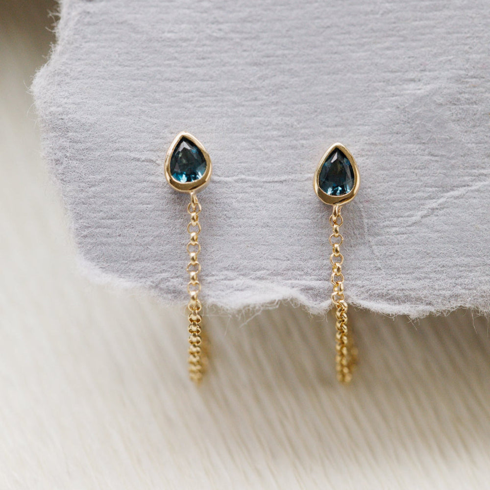 Gold earrings with blue gemstones on a soft fabric background