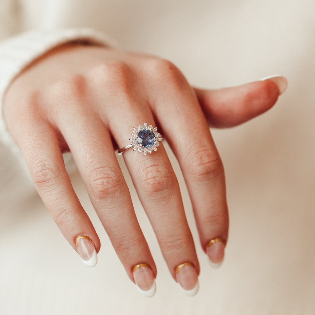 Hand wearing a ring with a blue sapphire gemstone on a neutral background