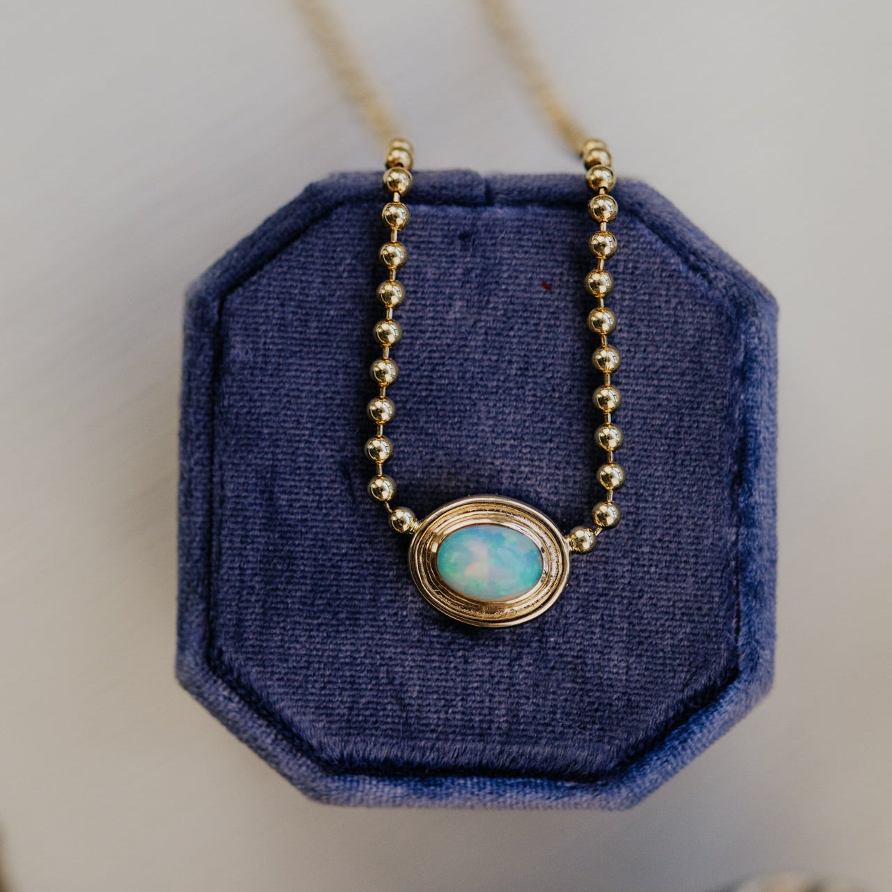 Necklace with a blue opal pendant on a blue cushion against a neutral background