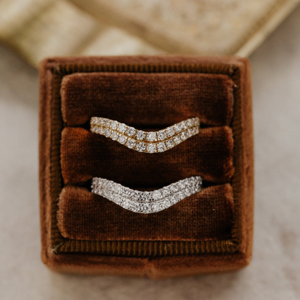 Two rose diamond tracer bands in yellow and white gold in a brown velvet box on a textured surface.