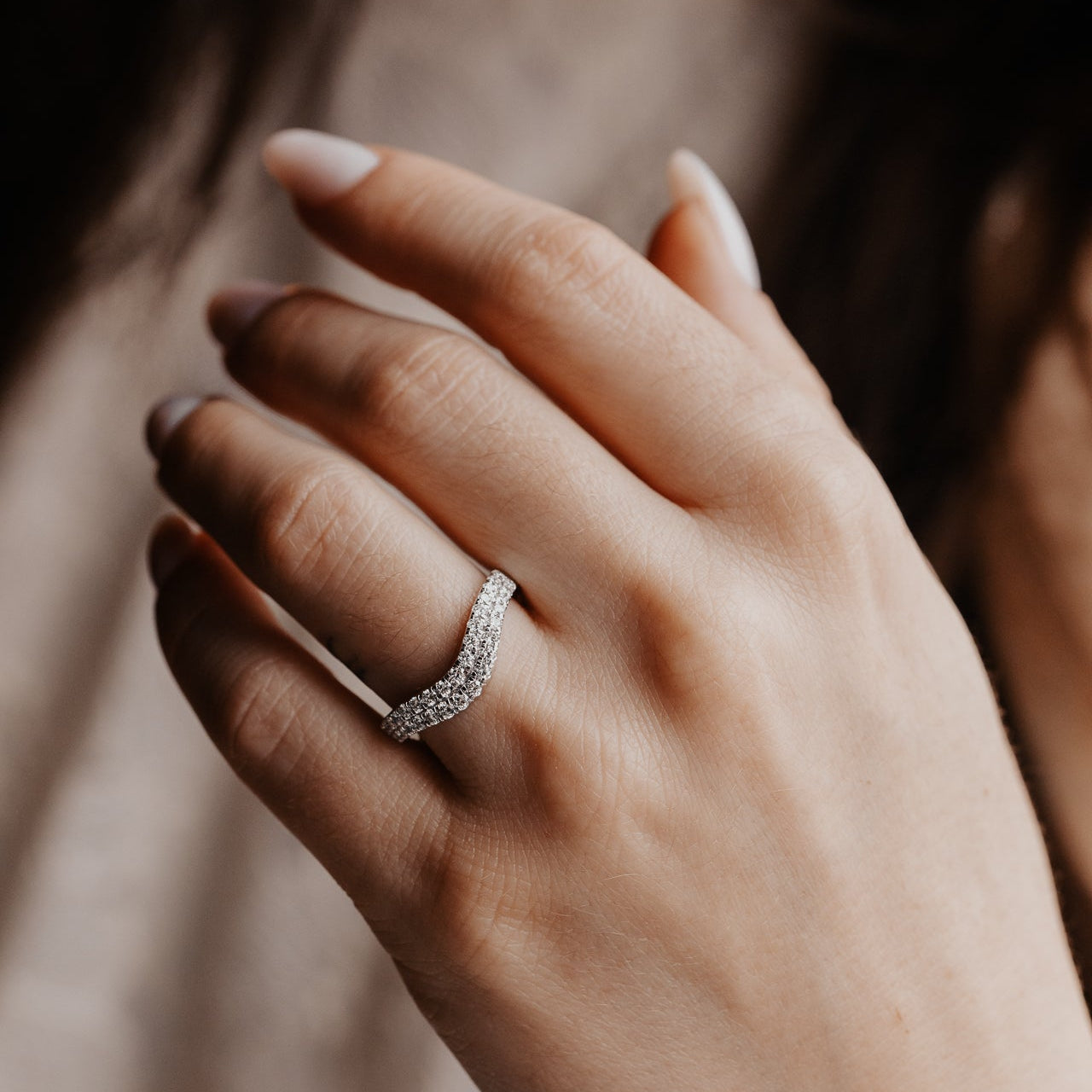 Close-up of a hand wearing a rose diamond tracer wedding band with a blurred background.